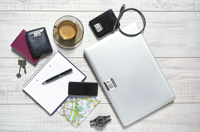 View of a wooden table with a laptop, external hdd, usb cable, mobile, notebook, pen, watch, wallet, passport, map, keys and a cup of coffee on it
